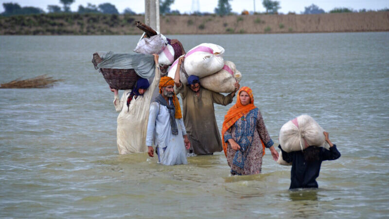 2022年8月24日，巴基斯坦西南部俾路支省贾法拉巴德，一个流离失所的家庭涉水穿过洪水泛滥的地区