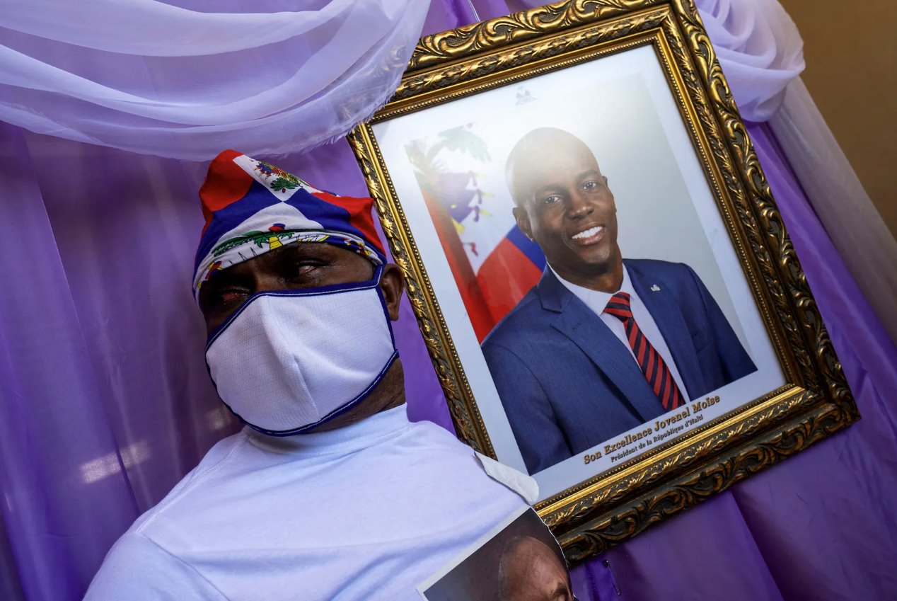 2021年7月22日，海地海地角市政厅的纪念碑上，一名男子站在被杀海地总统若弗内尔·莫伊兹的肖像旁边。