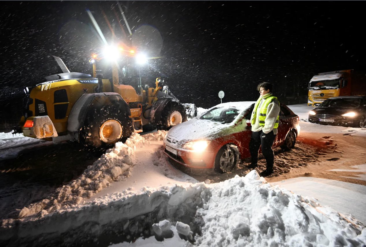 2024年1月4日，瑞典南部霍比和克里斯蒂安斯塔德之间的E22高速公路Ekerodsrasten上，轮式装载机清除了积雪，汽车和卡车被回收，人员被家园卫队的履带式车辆疏散。