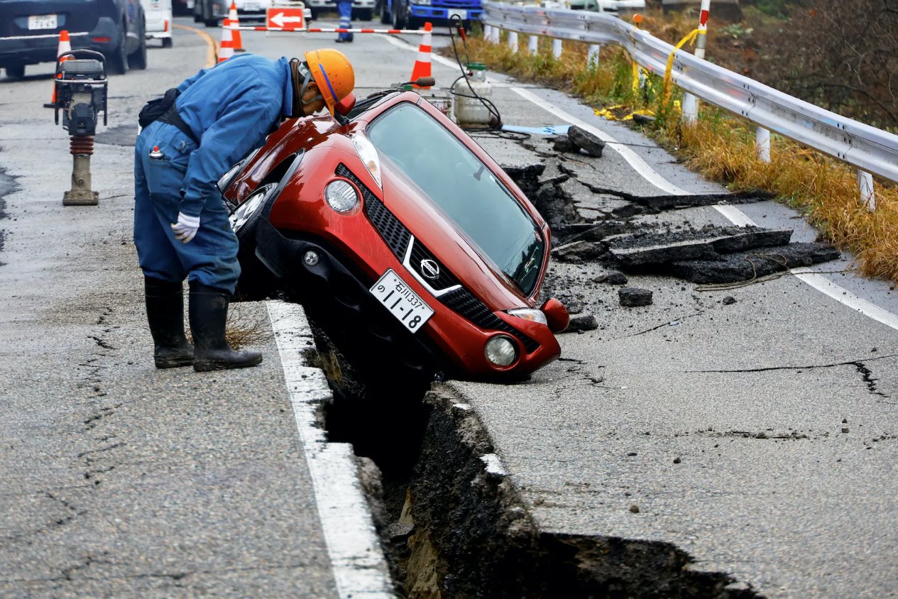 2024年1月3日，日本穴水附近，一名工人正在查看地震后困在破损道路上的汽车。