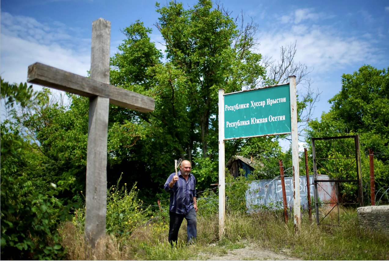 2018年6月4日，格鲁吉亚德瓦尼，57岁的当地居民马拉布·梅卡里什维利(MarabMekarishvili)走过格鲁吉亚南奥塞梯分离地区事实上的边界线上的“南奥塞梯共和国”横幅。